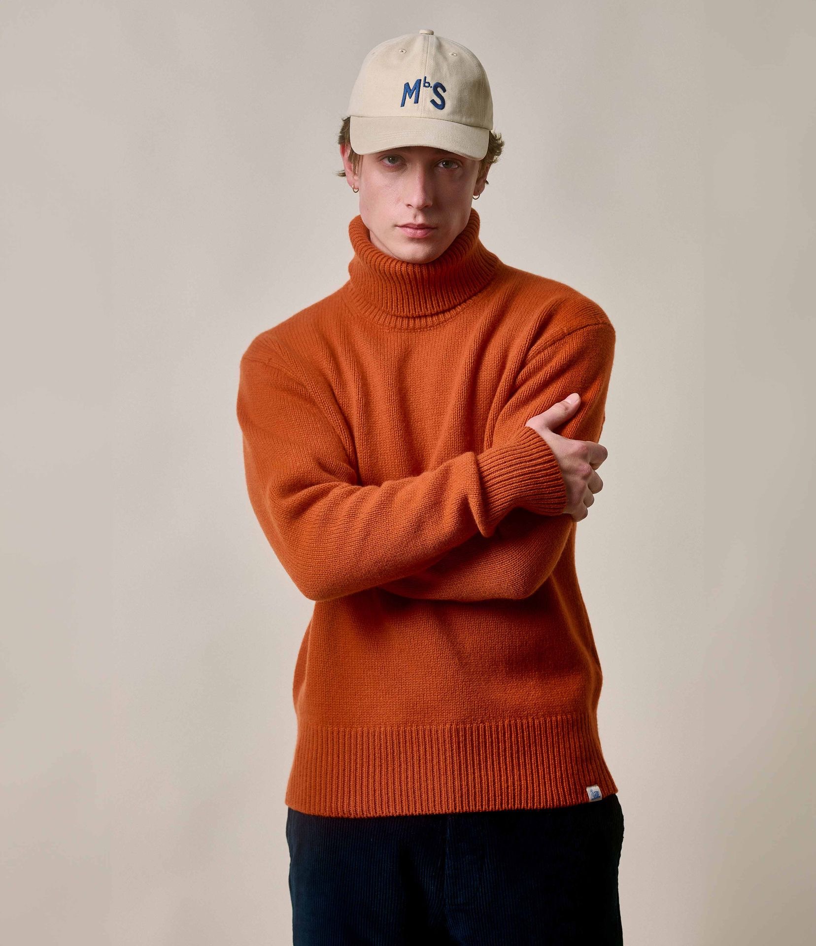 man wearing knitted turtleneck pullover and mbs logo cap