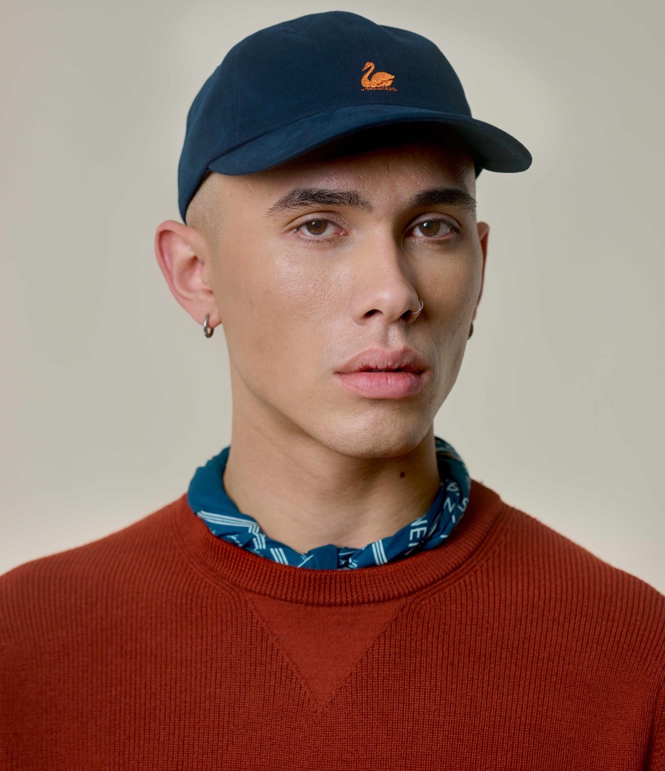 man wearing blue swan logo cap, blue bandana and red knitted pullover