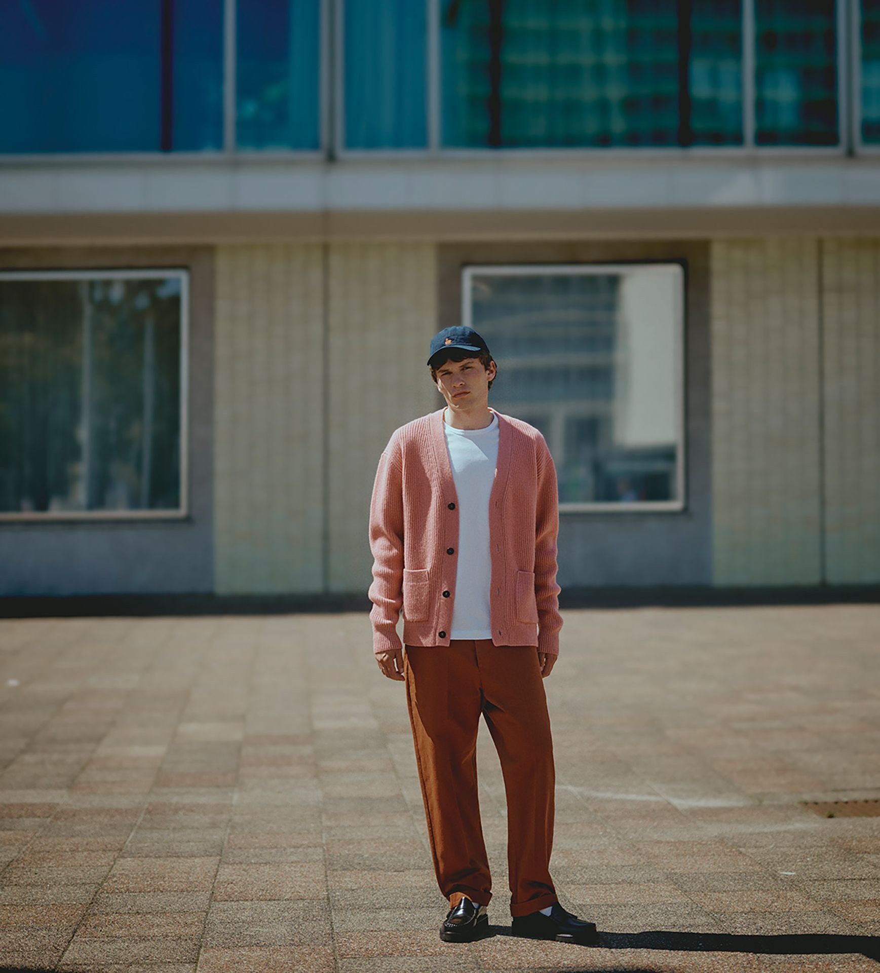 Man wearing white T-shirt, pink knit cardigan, chino pants and blue cap