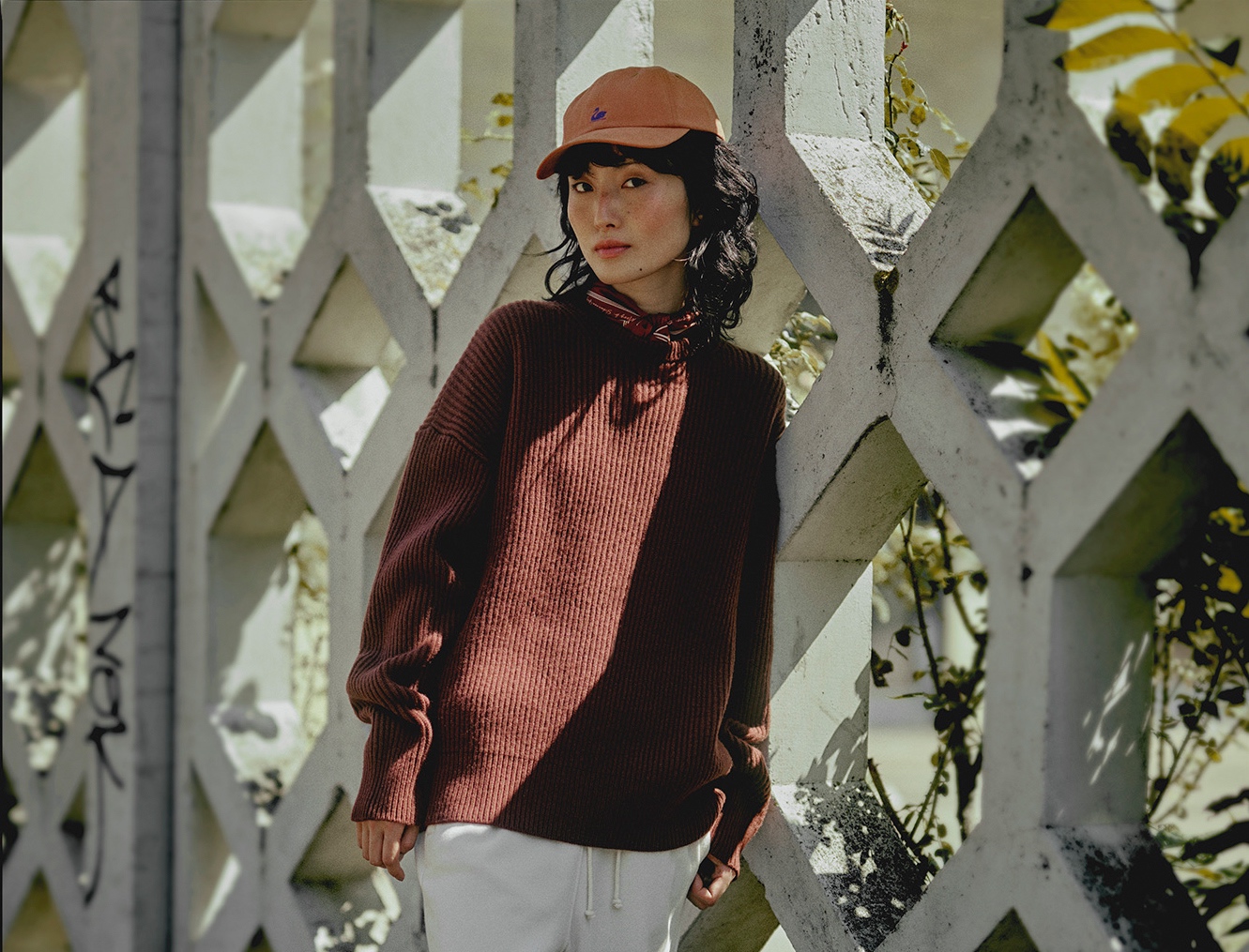 Woman wearing burgundy knit pullover, white sweatpants, bandana and orange cap