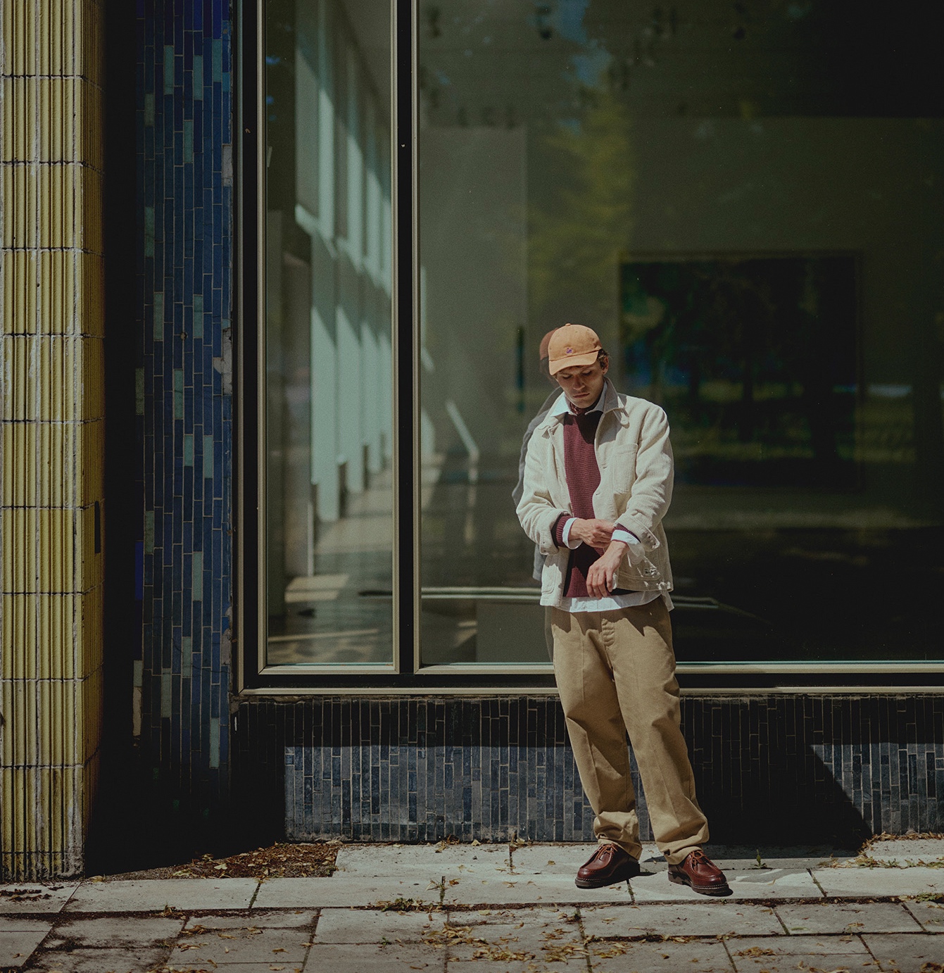 Man with orange cap and bandana wearing burgundy waffle pullover and white corduroy jacket over white shirt 