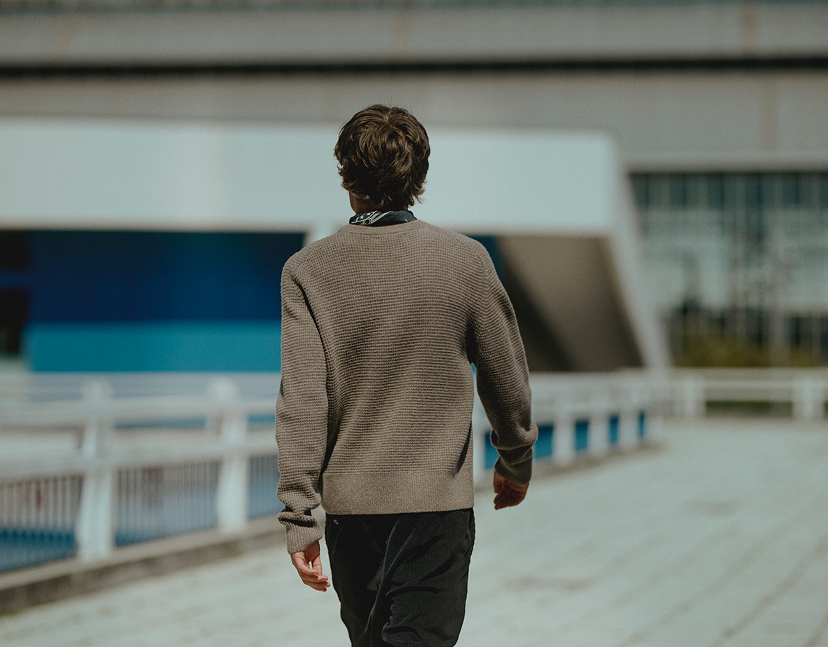 Man with grey waffle pullover and black chino walking away