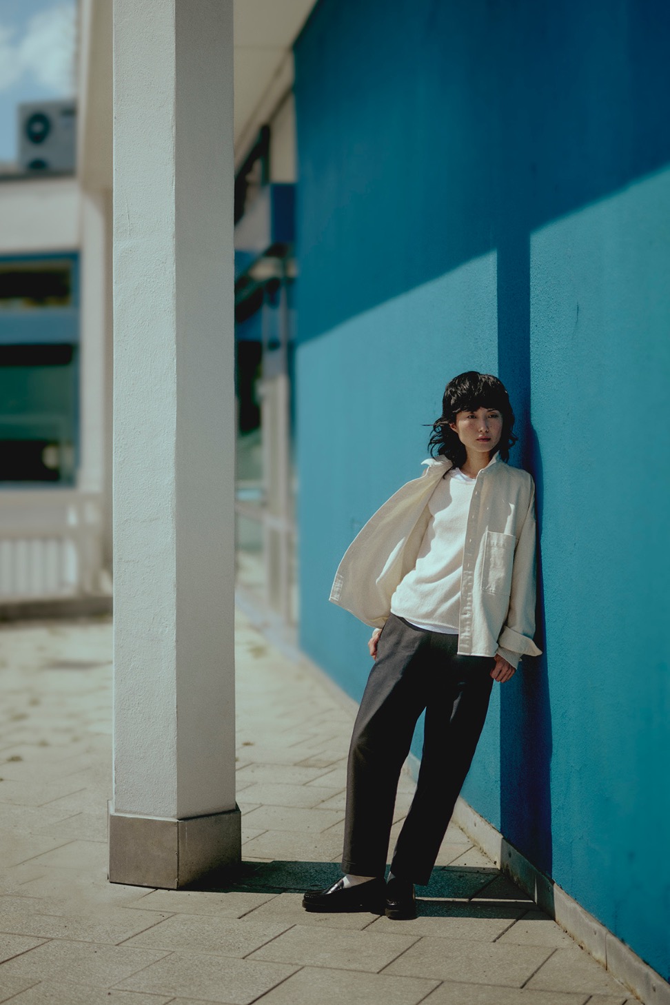 Woman wearing off-white overshirt and crewneck pullover in front of a blue wall