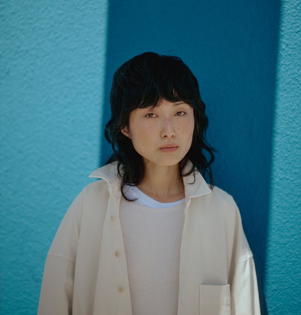 Woman wearing off-white overshirt and crewneck pullover in front of a blue wall