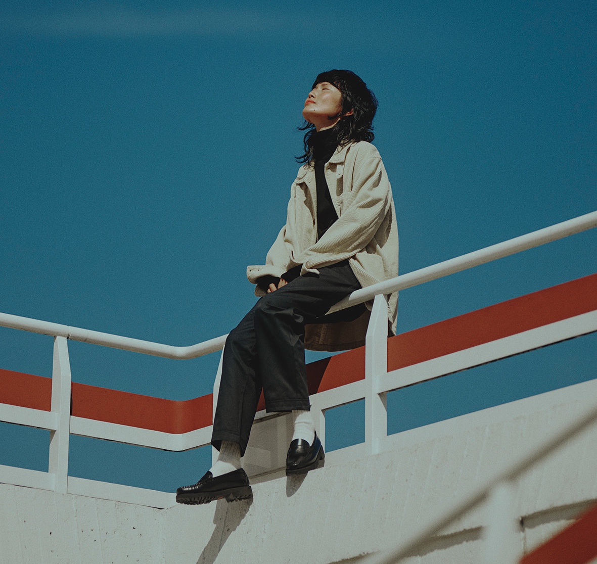 Woman wearing white corduroy jacket over black turtleneck pullover in front of the blue sky