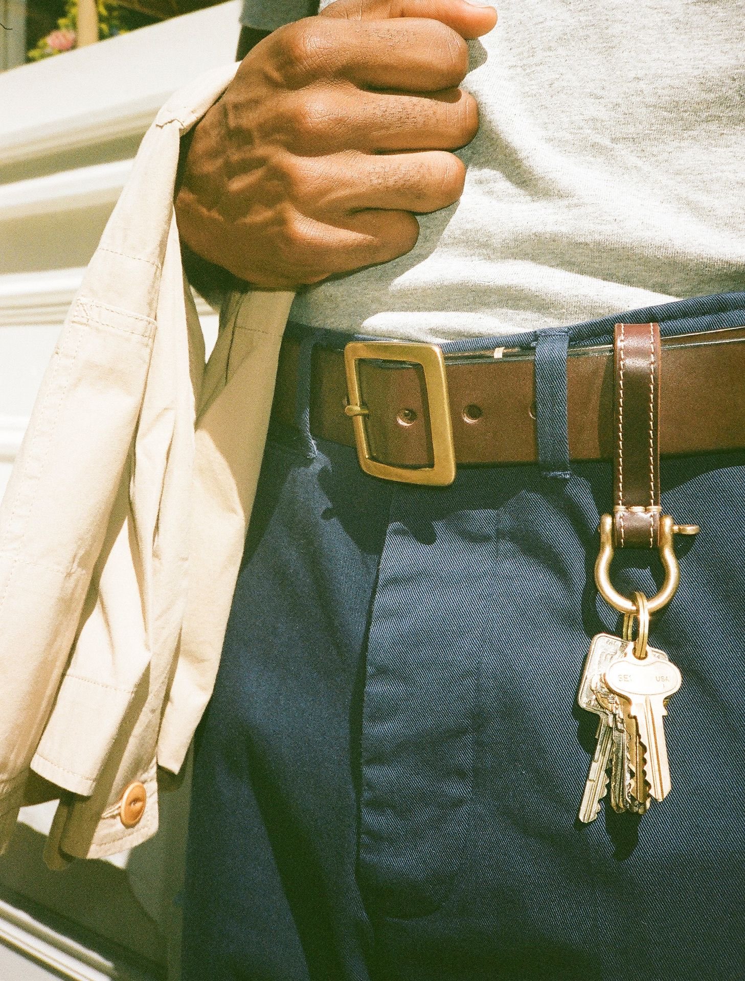 Closeup of a man wearing brown leather belt and keychain on blue chino trousers