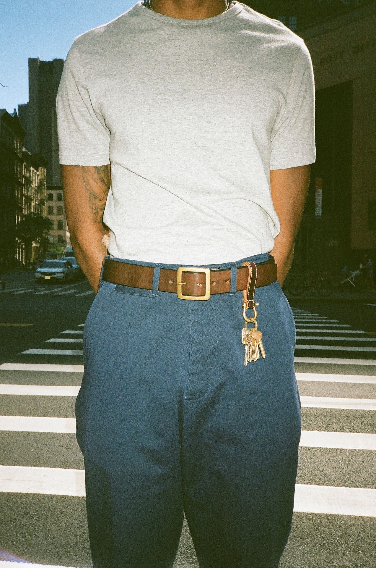 Man on crosswalk wearing brown leather belt and keychain on blue chino trousers