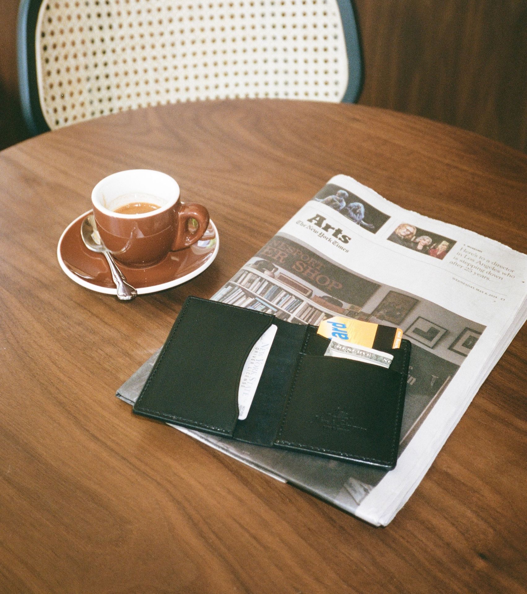 Black leather cardholder next to coffee and newspaper on a table