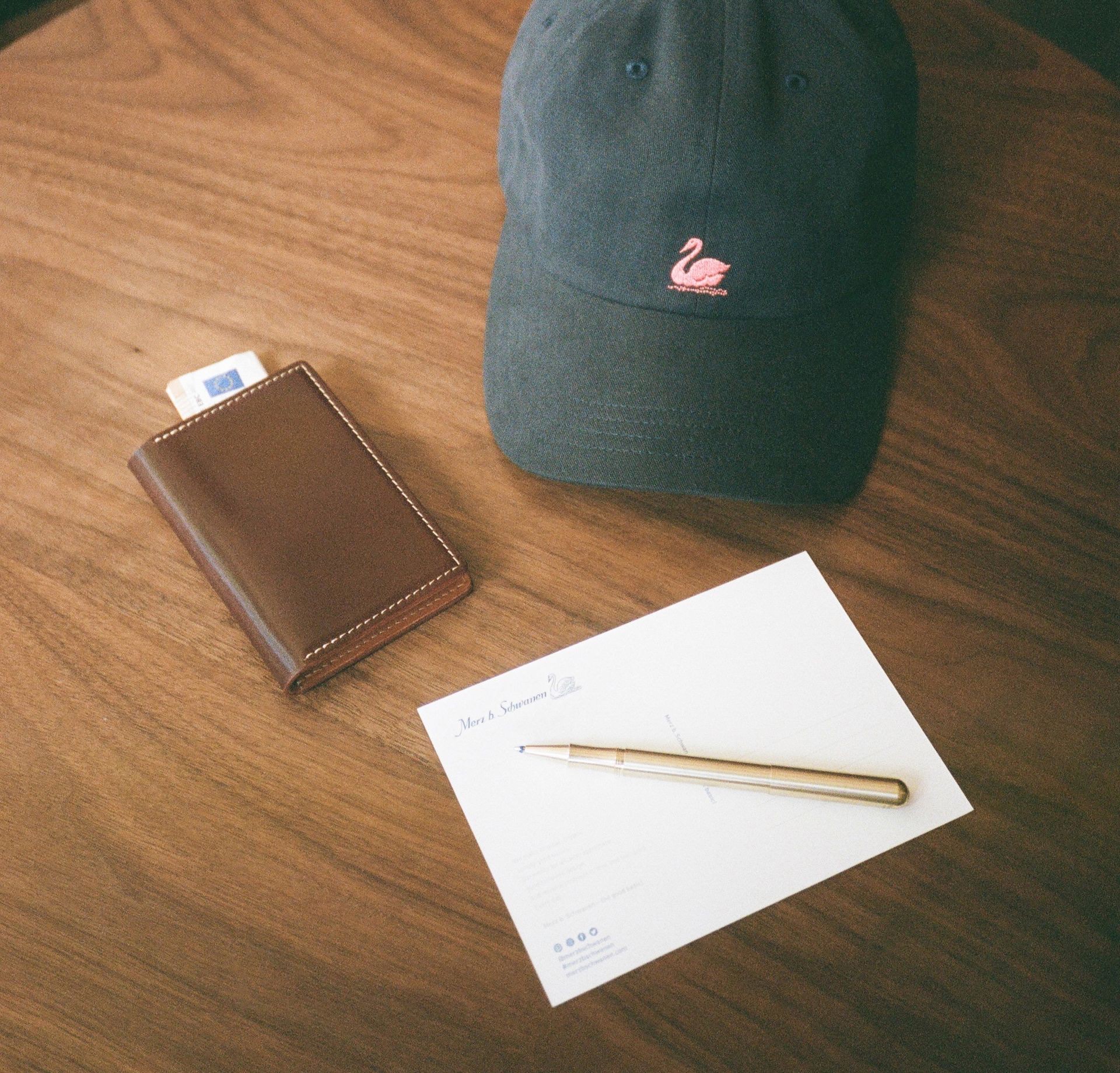 Brown leather cardholder next to grey cap and metal pen on a table