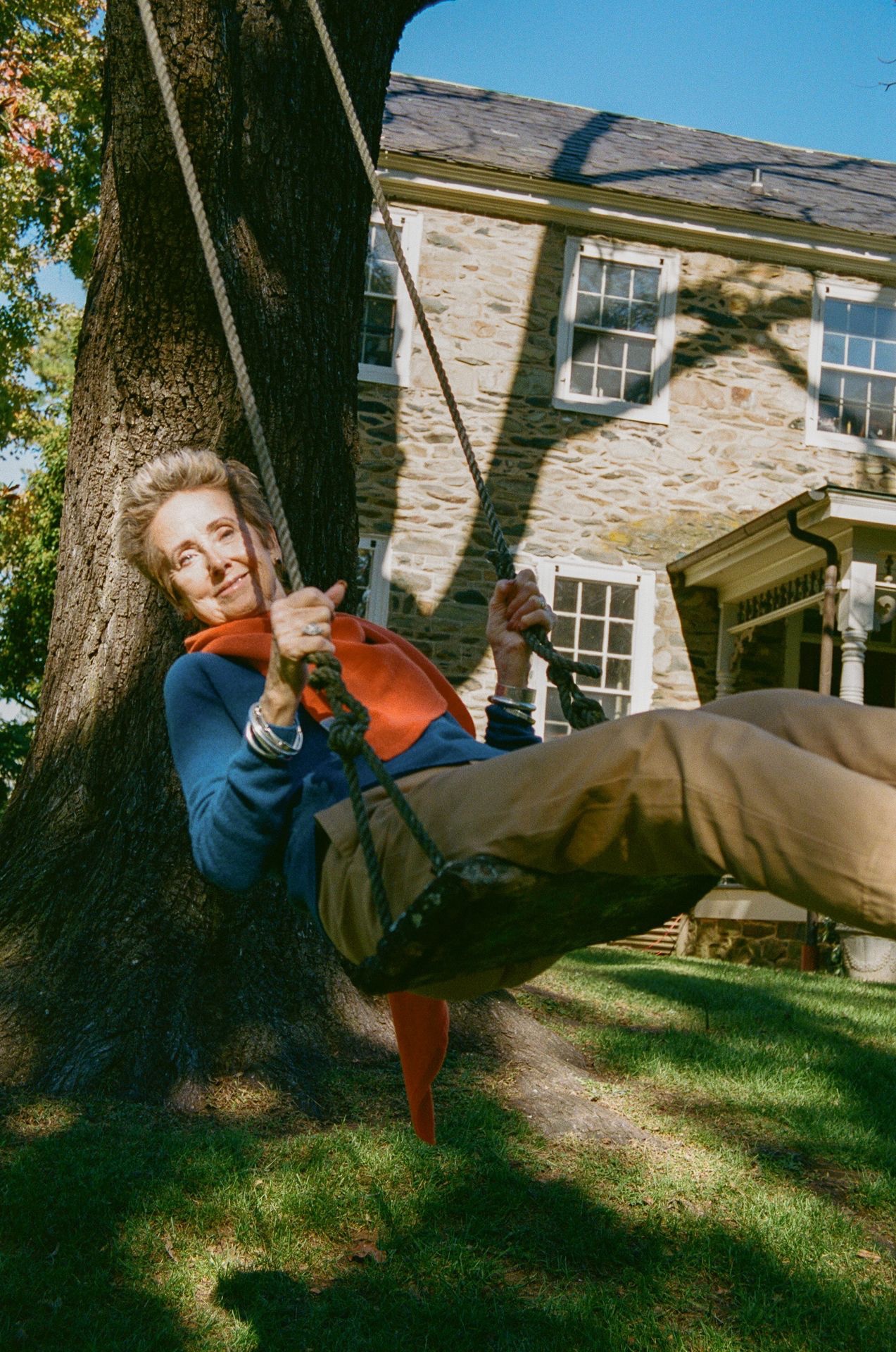 Woman on swing wearing blue pullover, orange scarf and beige chino trousers