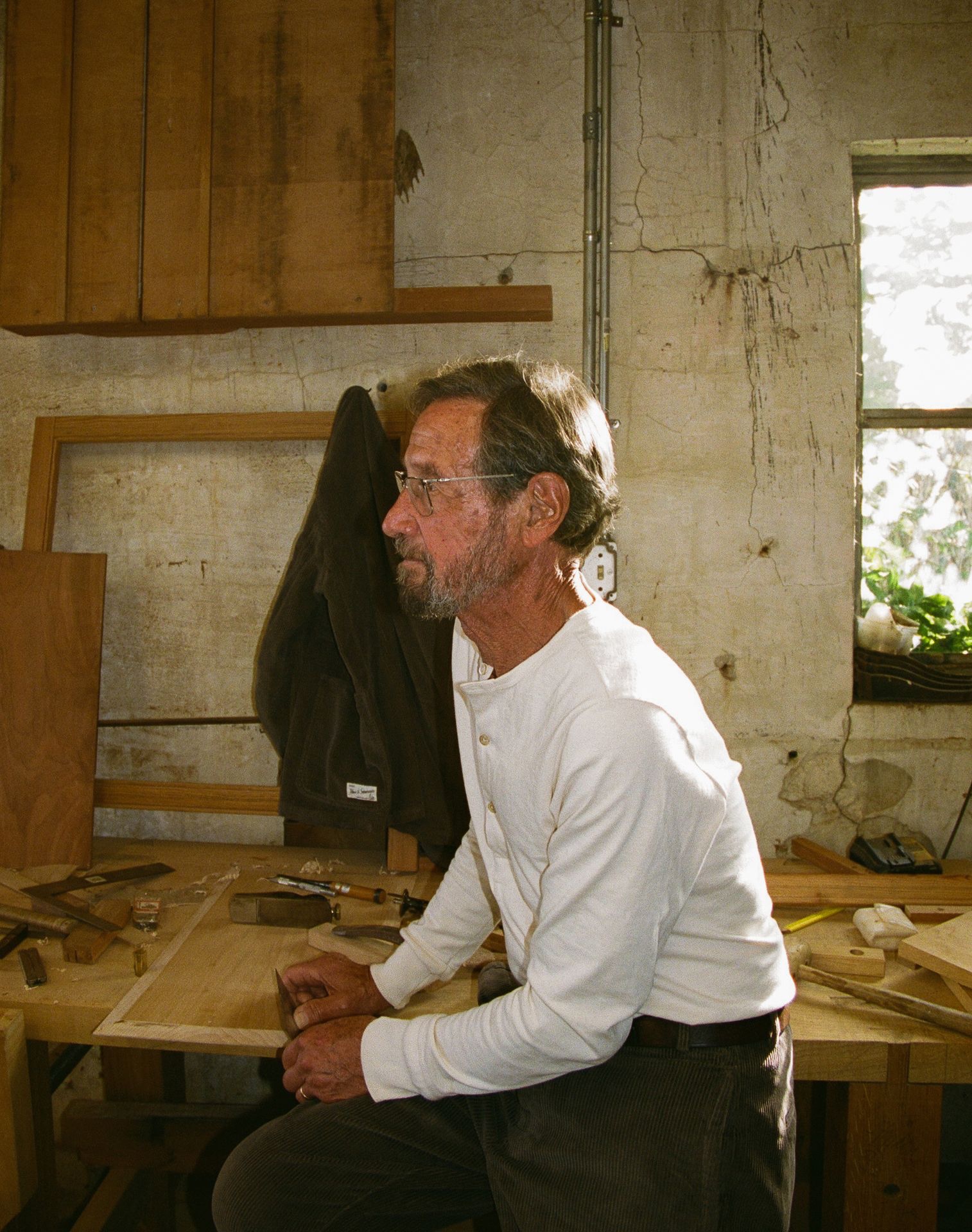 Man in his workshop wearing white longsleeved henley and corduroy trousers